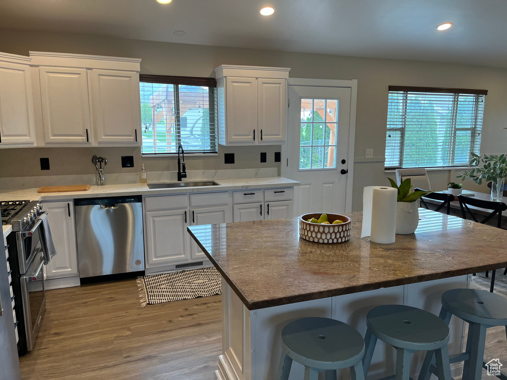 Kitchen with a center island, white cabinets, appliances with stainless steel finishes, sink, and light hardwood / wood-style floors
