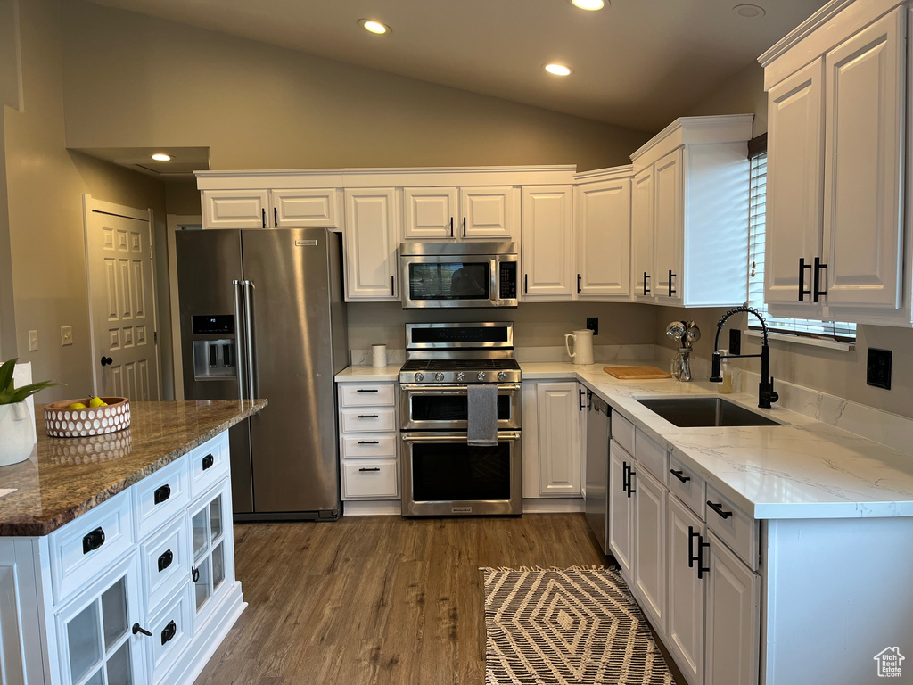 Kitchen with appliances with stainless steel finishes, lofted ceiling, hardwood / wood-style flooring, white cabinetry, and sink