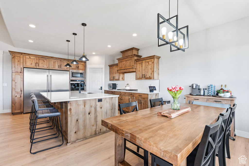 Kitchen featuring built in appliances, light hardwood / wood-style floors, hanging light fixtures, a kitchen island with sink, and an inviting chandelier