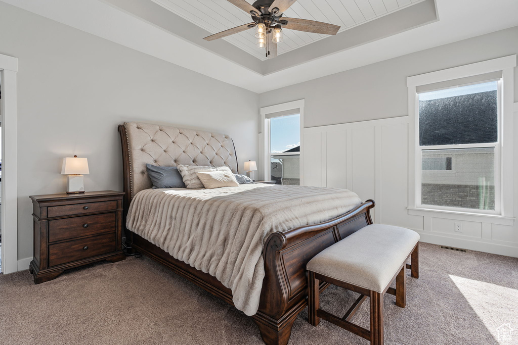 Bedroom with light carpet, a raised ceiling, and ceiling fan