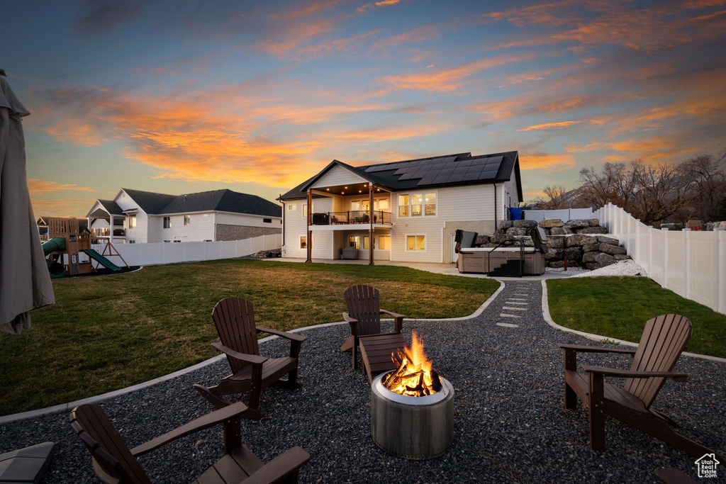 Back house at dusk with a playground, a patio, solar panels, an outdoor living space with a fire pit, and a lawn