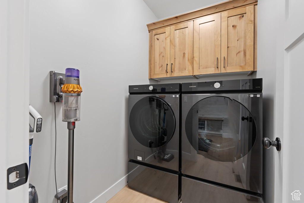 Clothes washing area with cabinets, independent washer and dryer, and light hardwood / wood-style flooring