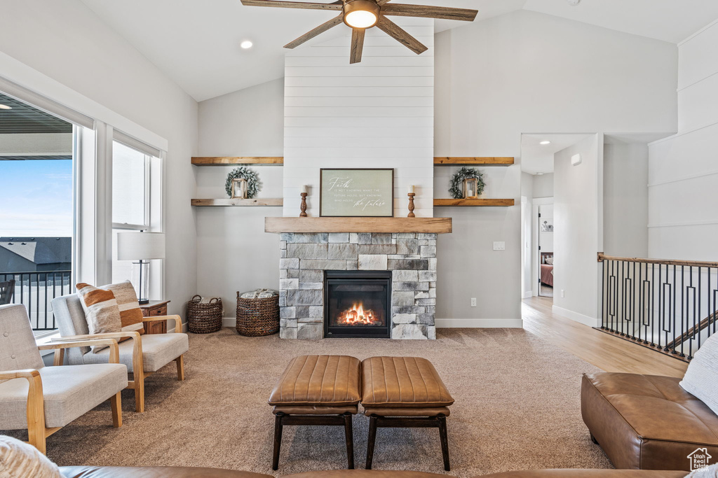 Carpeted living room featuring a stone fireplace, ceiling fan, and high vaulted ceiling