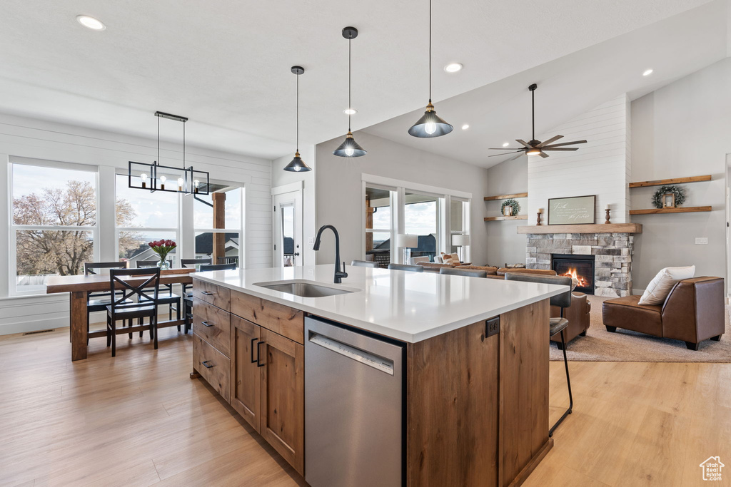 Kitchen with pendant lighting, light hardwood / wood-style flooring, dishwasher, a center island with sink, and a fireplace