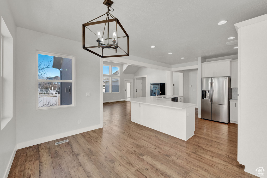 Kitchen featuring a chandelier, stainless steel fridge with ice dispenser, white cabinetry, hanging light fixtures, and light wood-type flooring