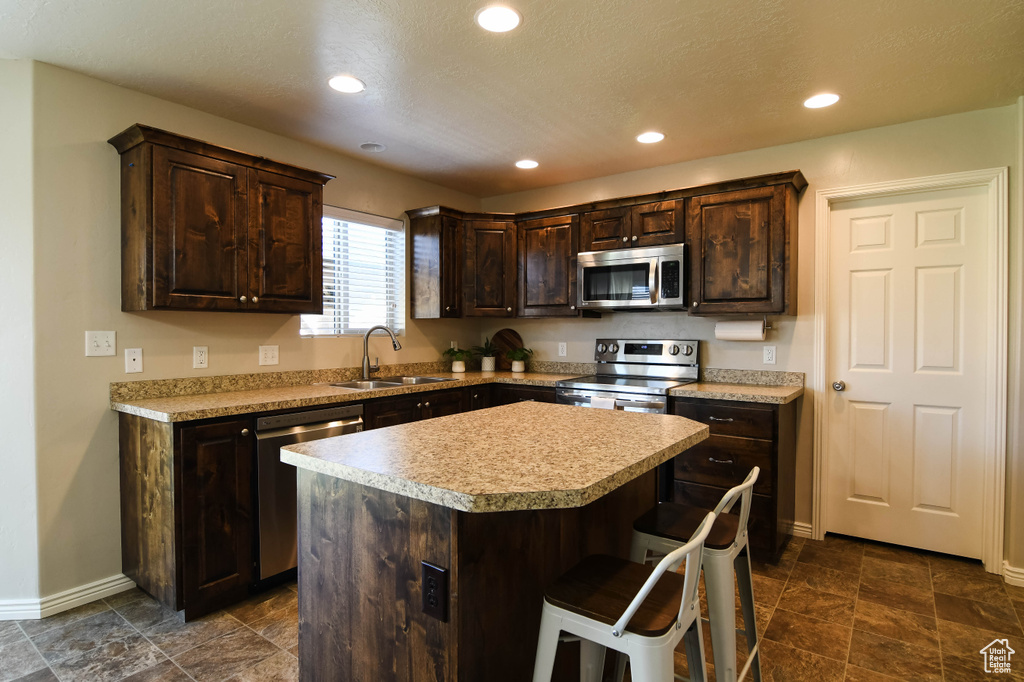 Kitchen featuring dark brown cabinetry, sink, appliances with stainless steel finishes, and a center island