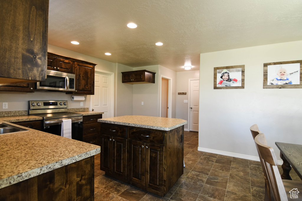 Kitchen featuring dark brown cabinetry, dark tile floors, stainless steel appliances, and a kitchen island