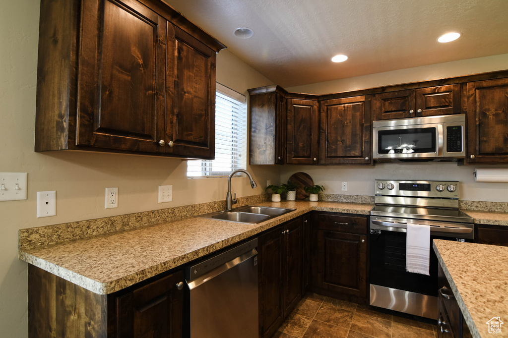 Kitchen featuring dark tile flooring, appliances with stainless steel finishes, dark brown cabinets, and sink