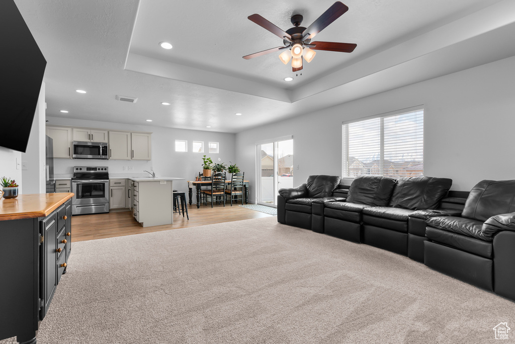 Carpeted living room with ceiling fan and a tray ceiling
