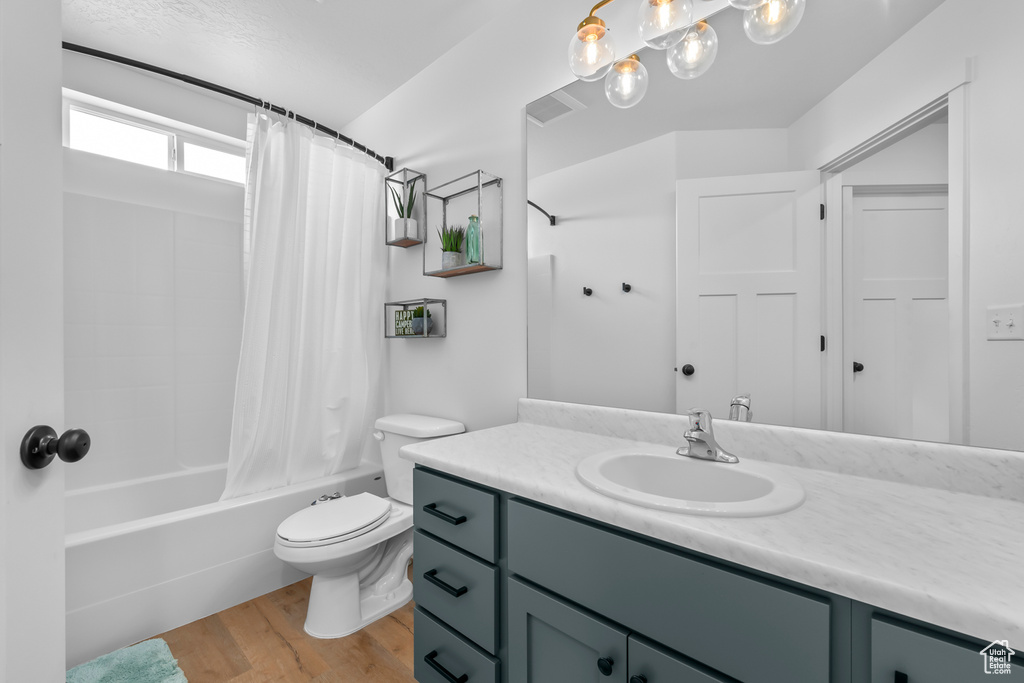 Full bathroom with toilet, oversized vanity, shower / bath combo with shower curtain, and hardwood / wood-style flooring