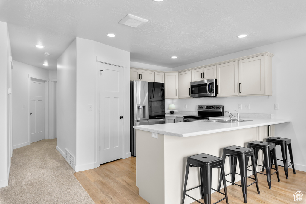 Kitchen with stainless steel appliances, kitchen peninsula, a breakfast bar, light carpet, and sink