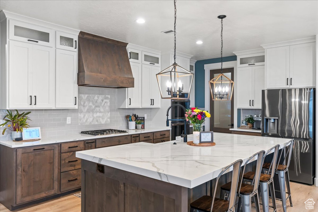 Kitchen with premium range hood, a center island with sink, and light hardwood / wood-style flooring