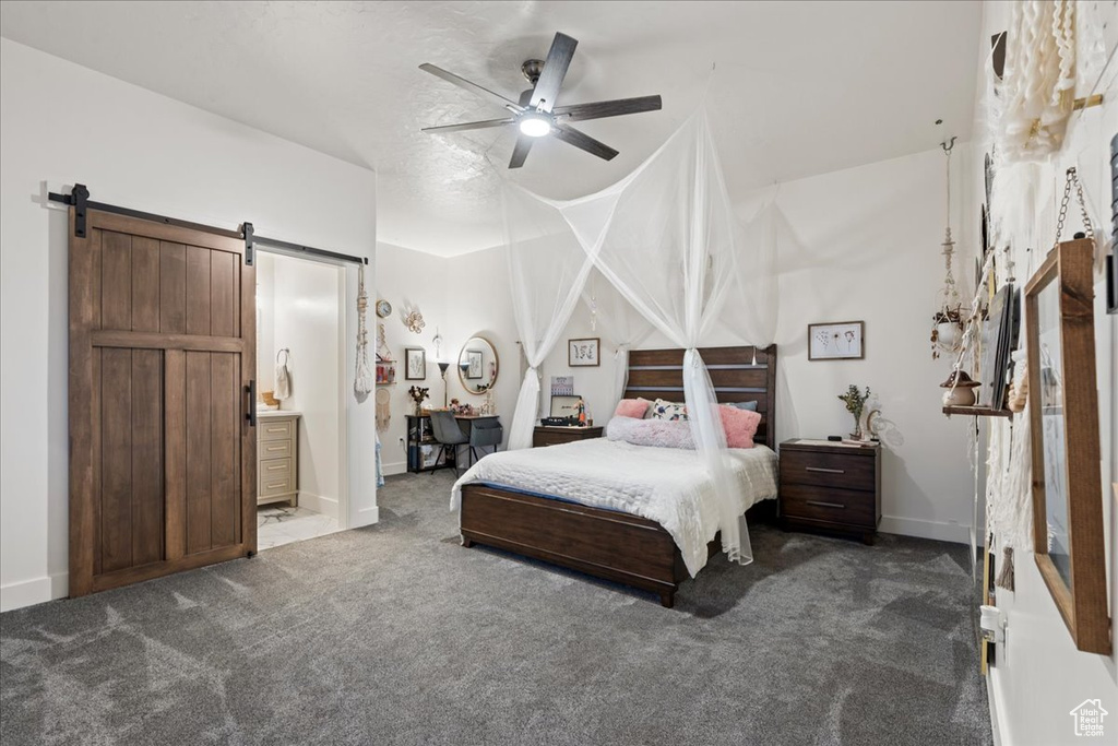 Carpeted bedroom with a barn door, connected bathroom, and ceiling fan