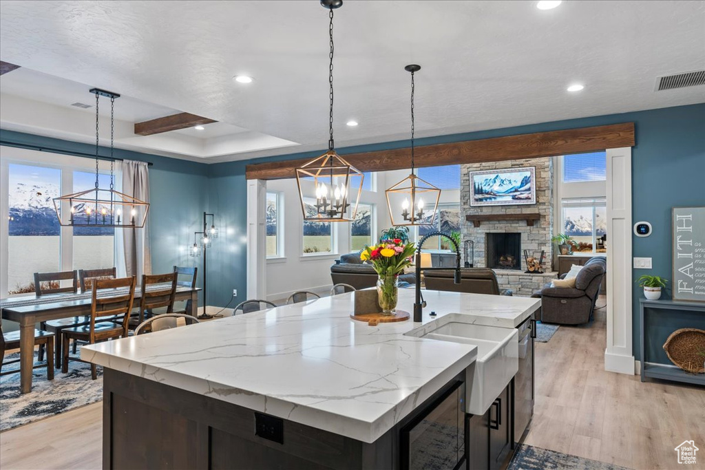 Kitchen with a fireplace, pendant lighting, light hardwood / wood-style flooring, and an island with sink