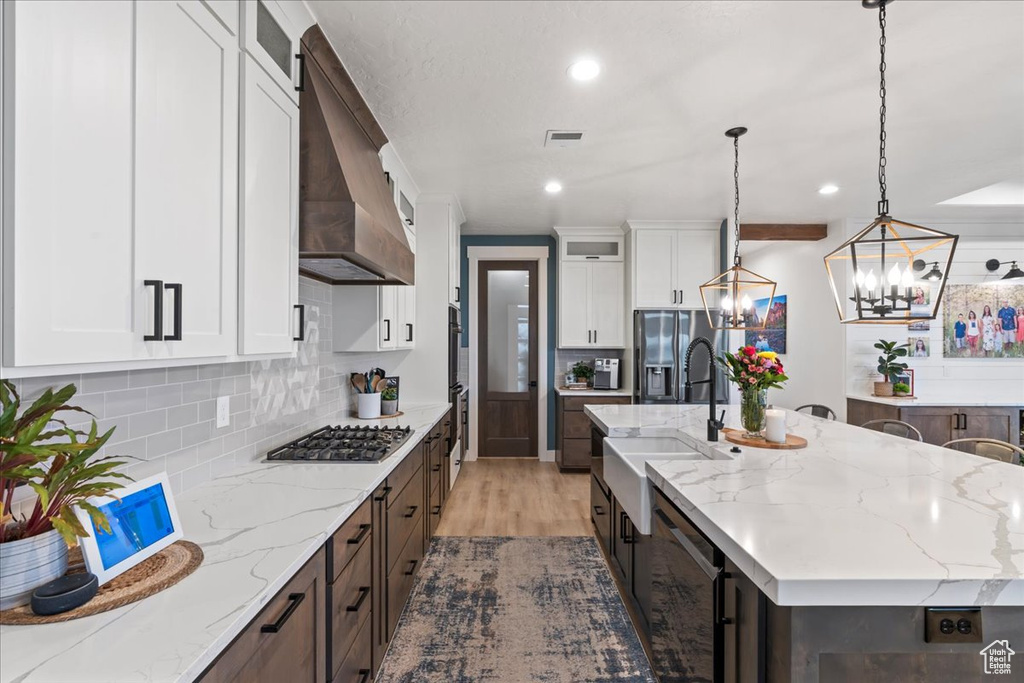 Kitchen with light stone countertops, white cabinetry, appliances with stainless steel finishes, wall chimney range hood, and hardwood / wood-style flooring