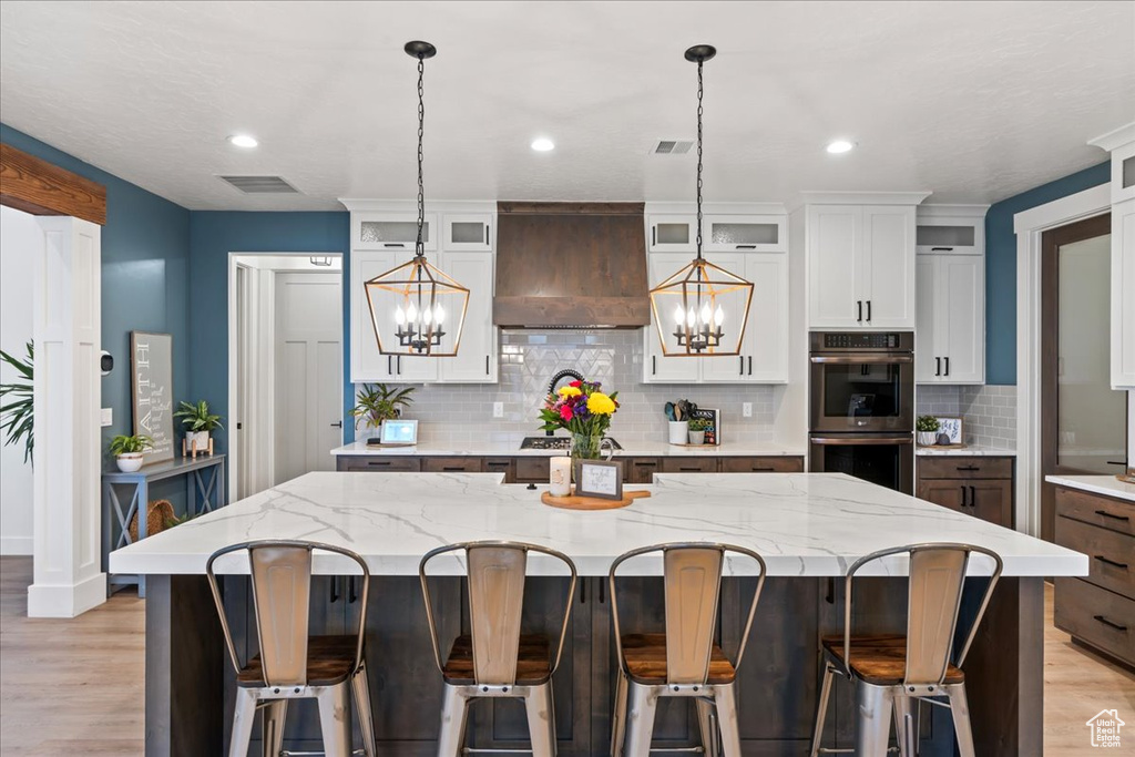 Kitchen featuring pendant lighting, appliances with stainless steel finishes, light hardwood / wood-style flooring, premium range hood, and a center island