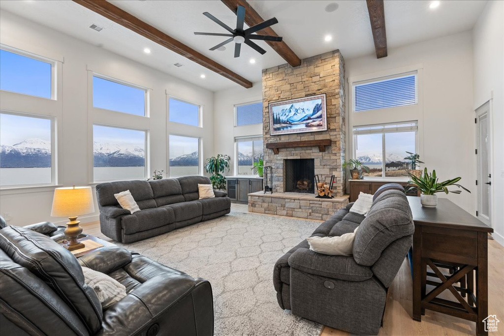 Living room with ceiling fan, a fireplace, a high ceiling, beam ceiling, and light wood-type flooring