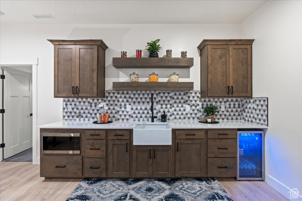 Bar featuring sink, stainless steel microwave, backsplash, light hardwood / wood-style floors, and wine cooler