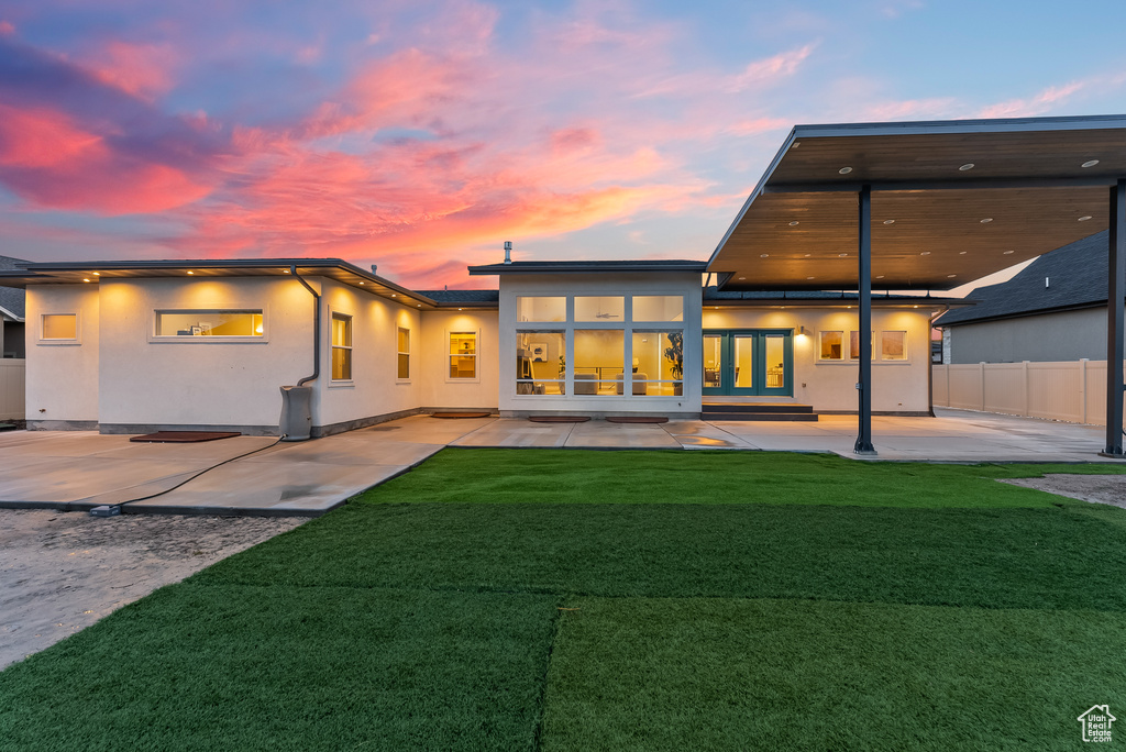 Back house at dusk featuring a lawn and a patio area