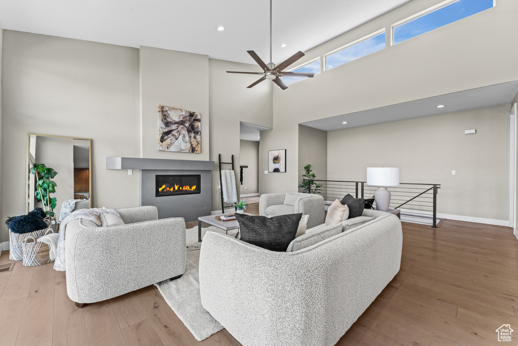 Living room featuring ceiling fan, a towering ceiling, and light hardwood / wood-style flooring
