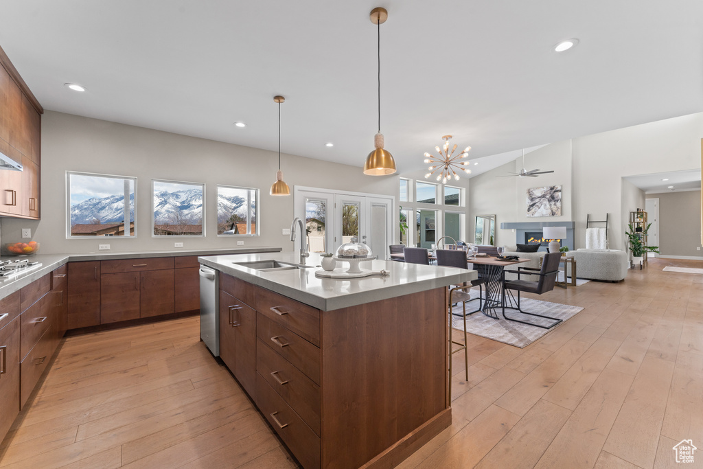 Kitchen with a kitchen island with sink, sink, light hardwood / wood-style flooring, decorative light fixtures, and a notable chandelier