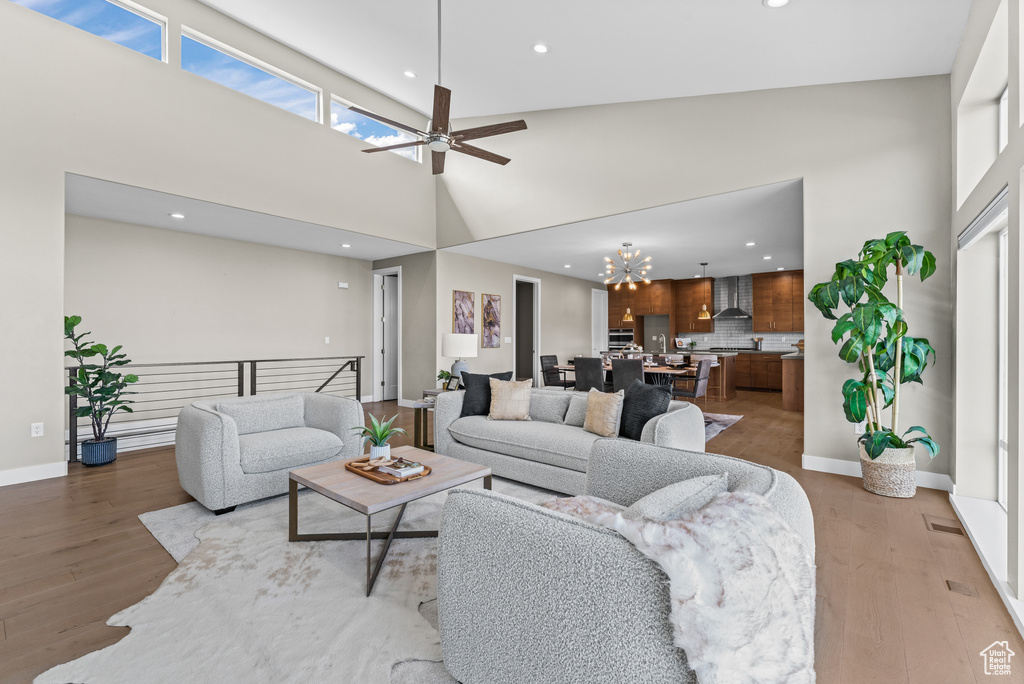 Living room featuring high vaulted ceiling, ceiling fan with notable chandelier, and light hardwood / wood-style flooring
