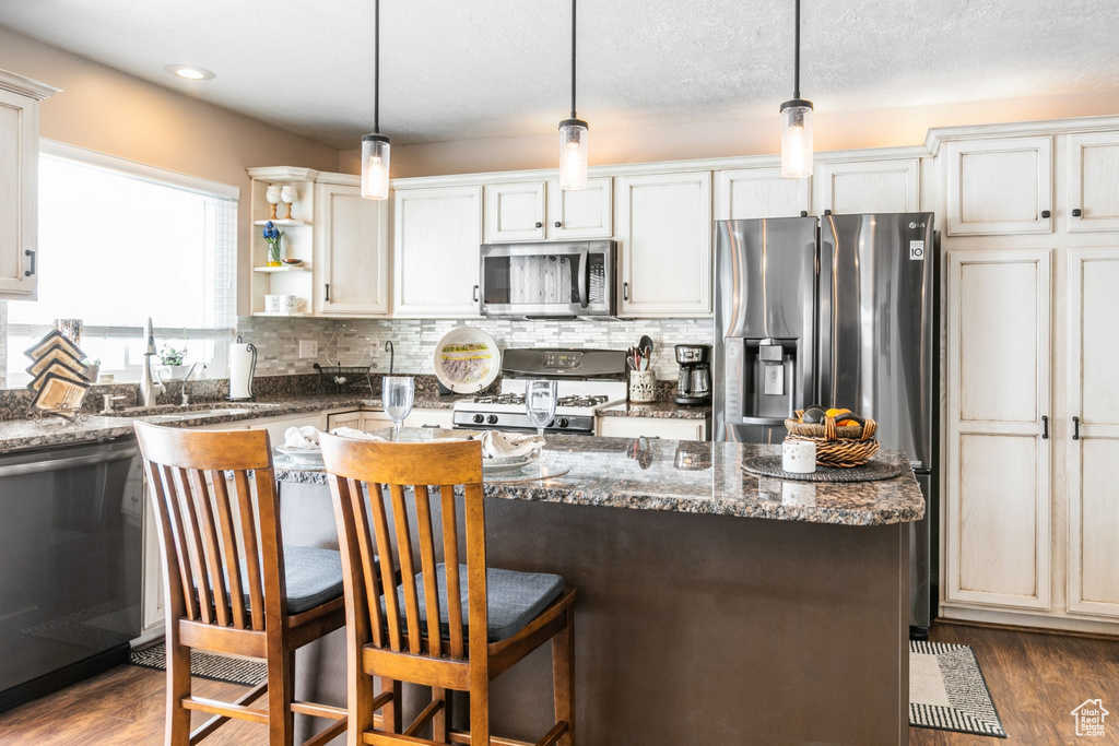 Kitchen featuring dark stone countertops, appliances with stainless steel finishes, decorative light fixtures, and dark hardwood / wood-style flooring