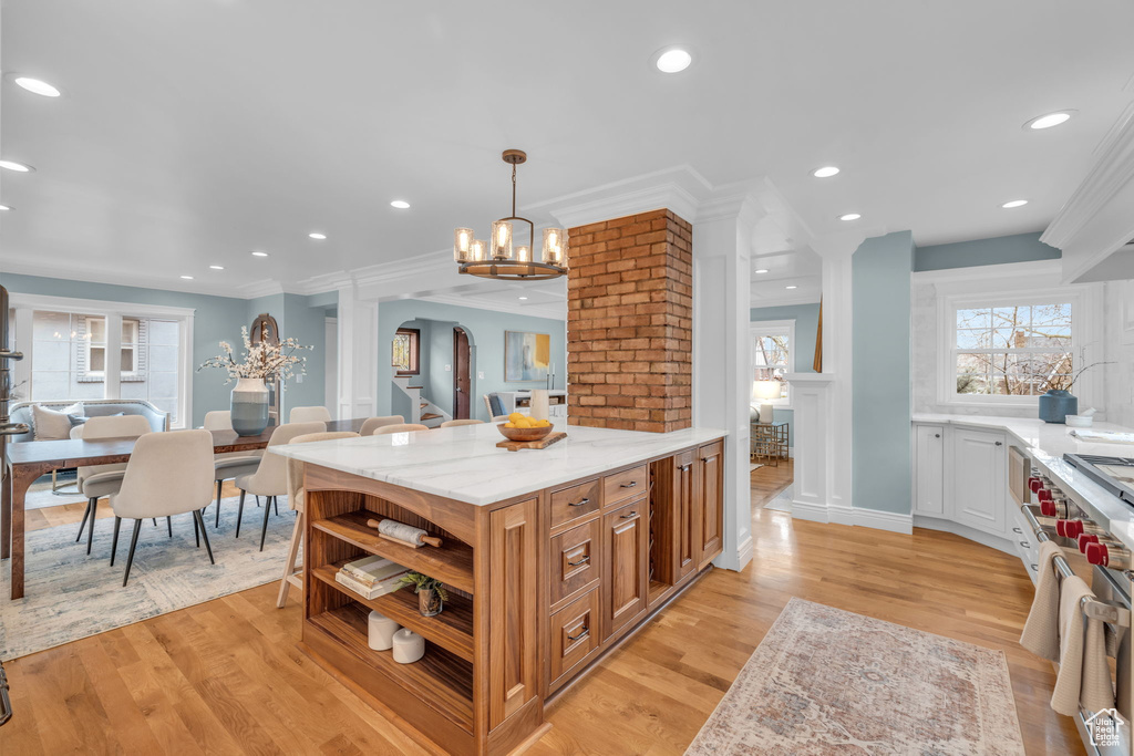 Kitchen with pendant lighting, crown molding, decorative columns, light stone countertops, and light wood-type flooring