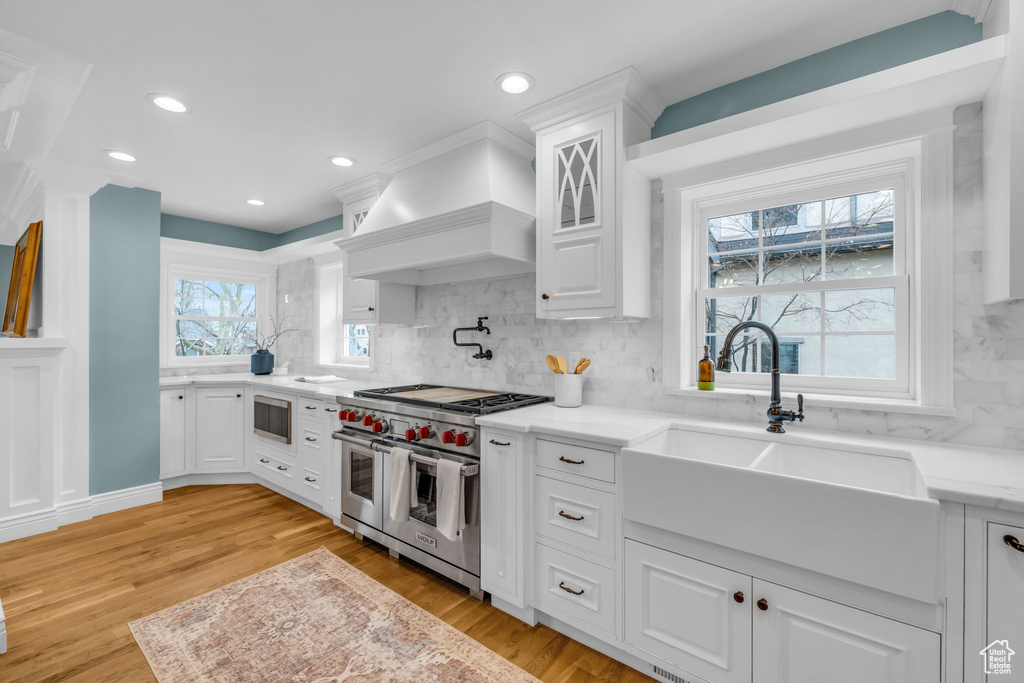 Kitchen featuring white cabinetry, light hardwood / wood-style floors, appliances with stainless steel finishes, and custom exhaust hood