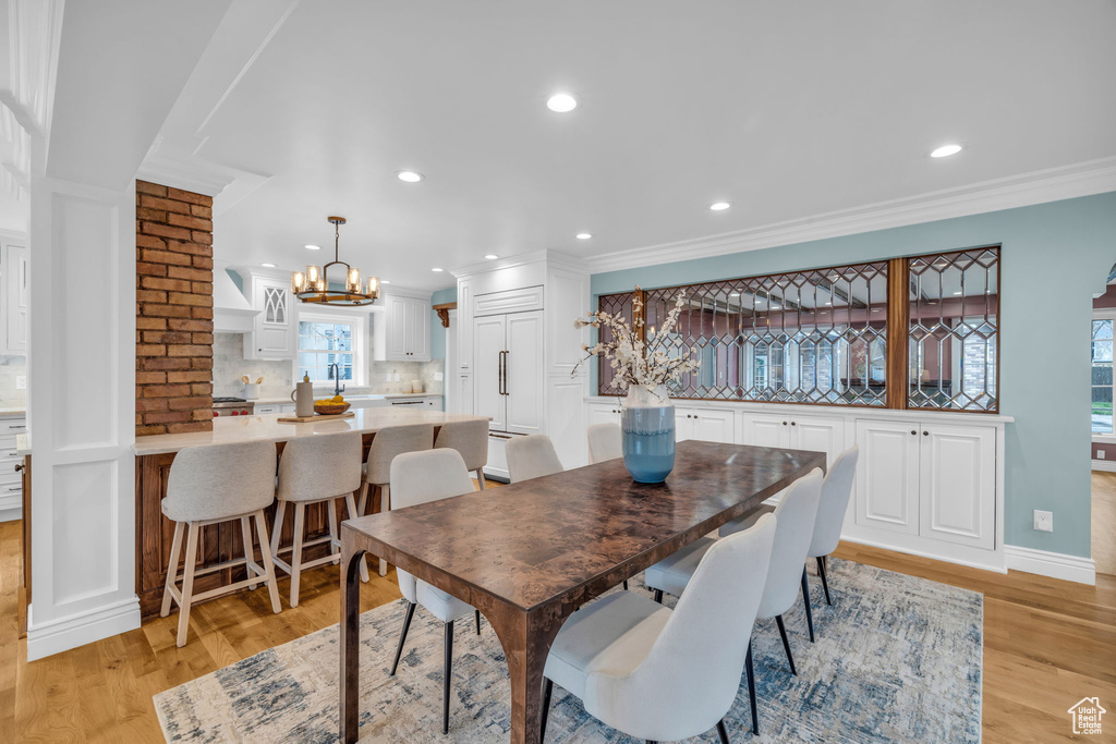 Dining space with a chandelier, brick wall, light wood-type flooring, and crown molding