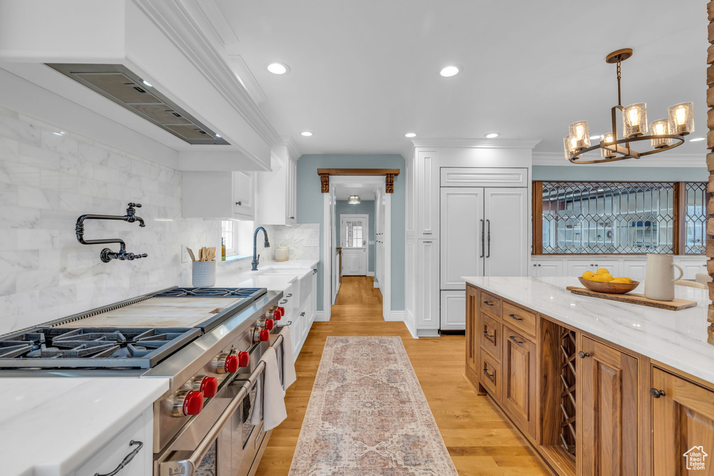 Kitchen featuring hanging light fixtures, white cabinets, premium appliances, tasteful backsplash, and light wood-type flooring
