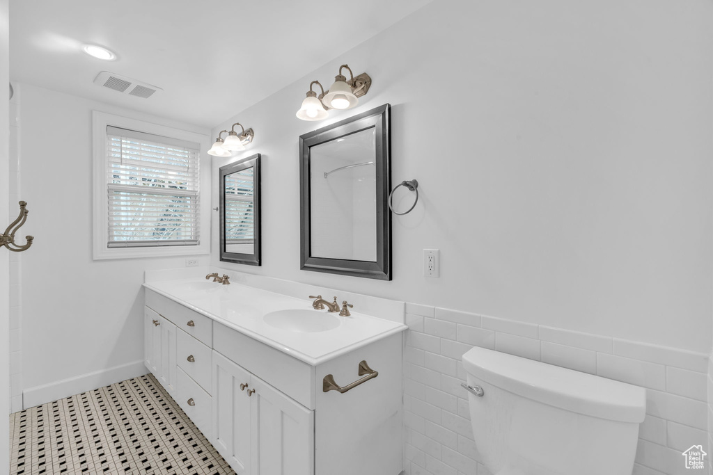 Bathroom featuring toilet, large vanity, dual sinks, and tile walls