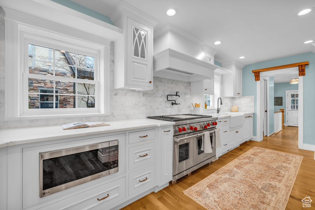 Kitchen featuring sink, light hardwood / wood-style flooring, stainless steel appliances, tasteful backsplash, and white cabinetry