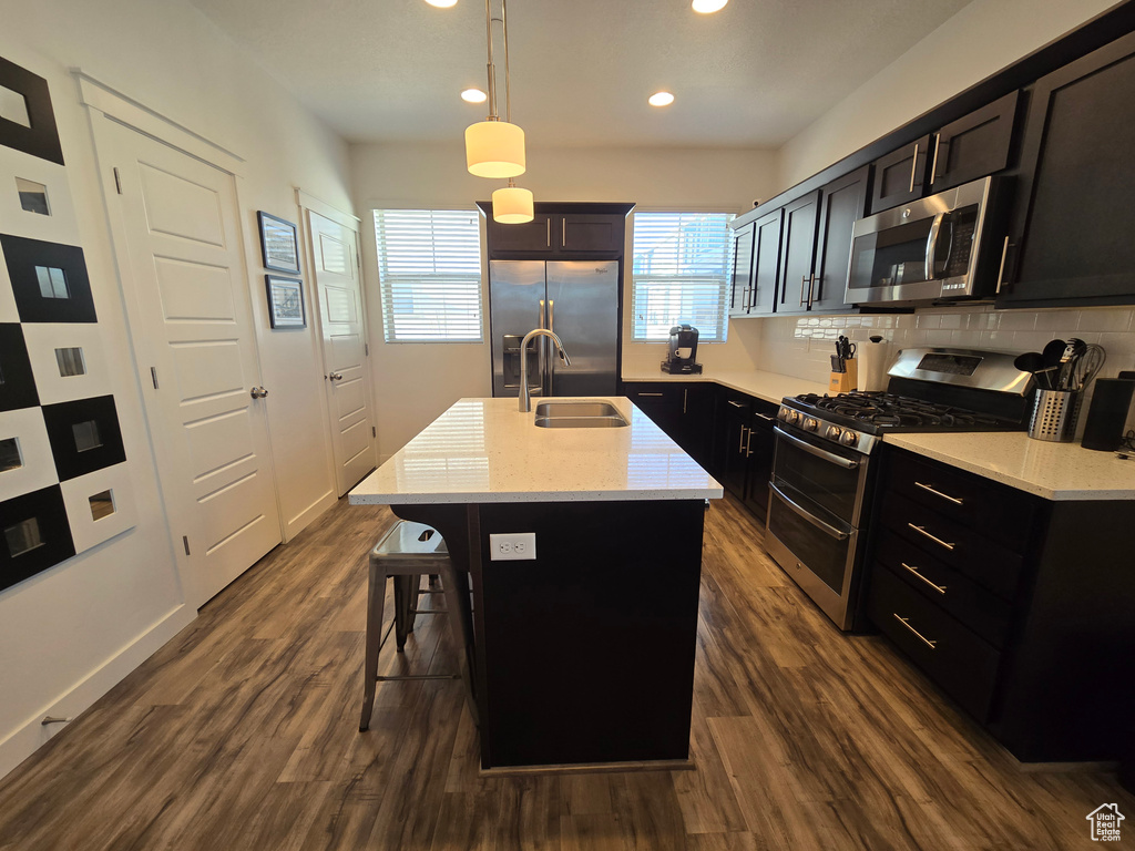 Kitchen with an island with sink, stainless steel appliances, decorative light fixtures, dark wood-type flooring, and a kitchen bar