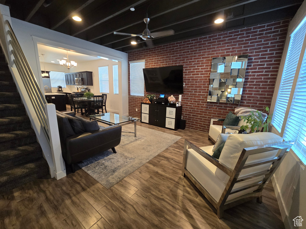 Living room featuring brick wall, dark hardwood / wood-style floors, and ceiling fan with notable chandelier