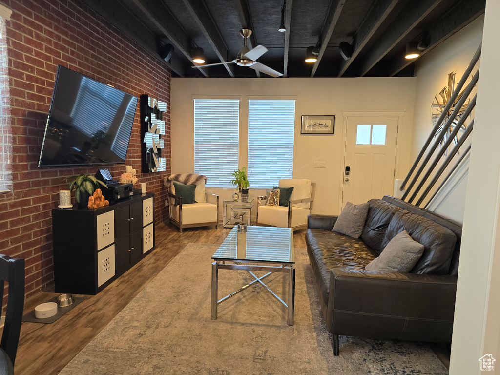 Living room featuring brick wall, ceiling fan, hardwood / wood-style flooring, and beamed ceiling