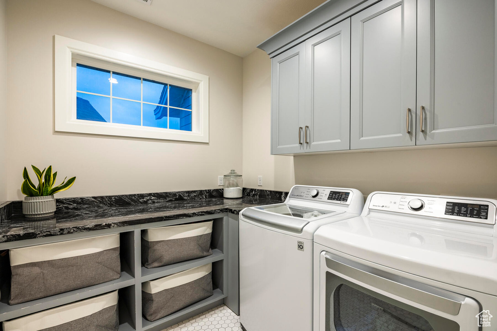 Laundry room with washer and dryer, light tile floors, and cabinets