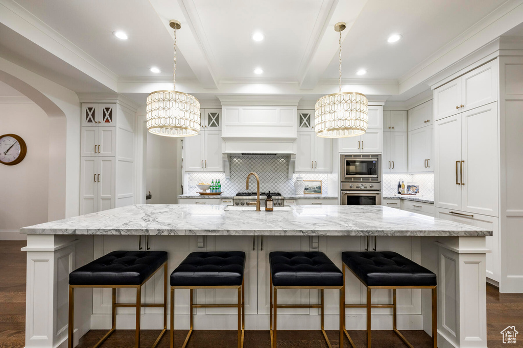 Kitchen featuring a kitchen island with sink, white cabinets, appliances with stainless steel finishes, dark wood-type flooring, and decorative light fixtures