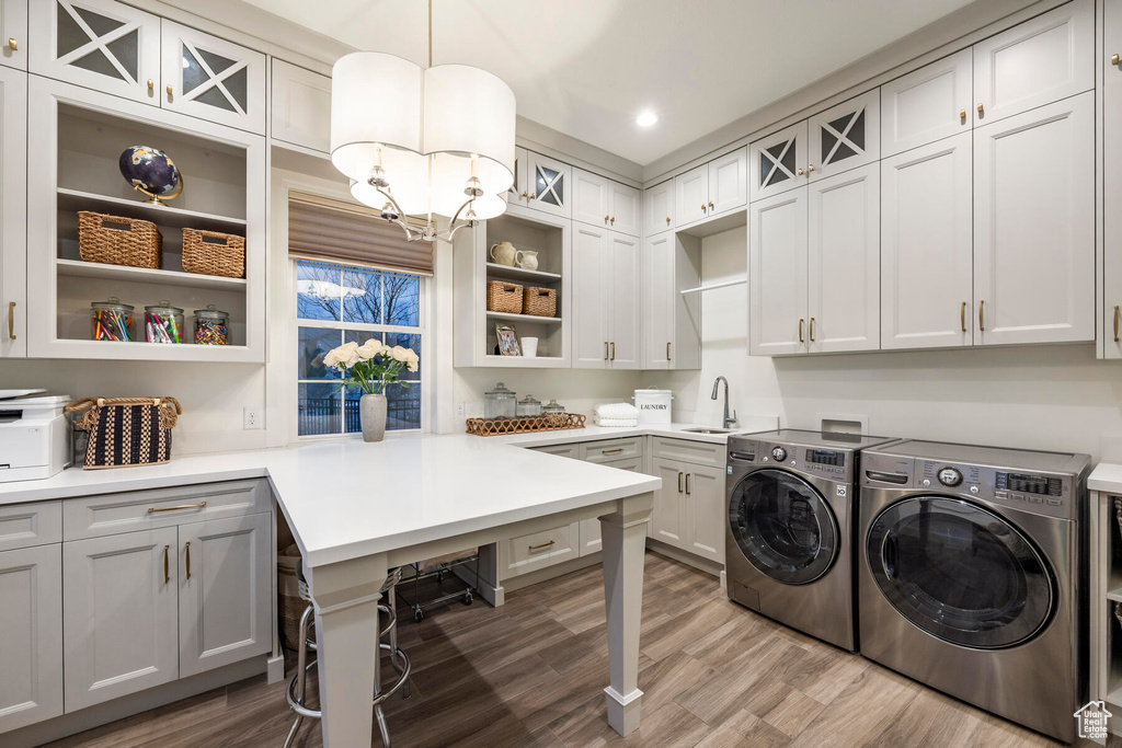Laundry room with a notable chandelier, washing machine and dryer, cabinets, and light hardwood / wood-style flooring