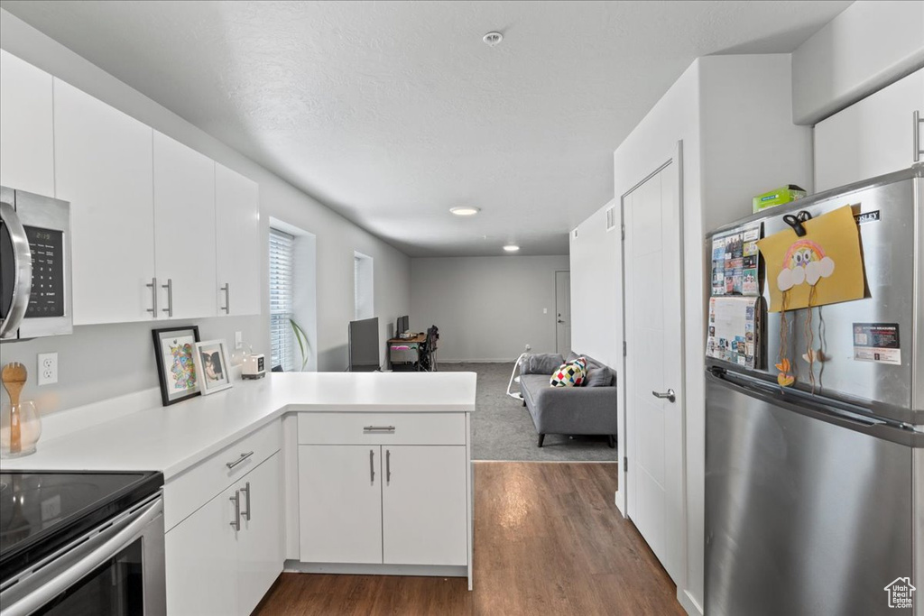 Kitchen with white cabinetry, kitchen peninsula, appliances with stainless steel finishes, and dark carpet