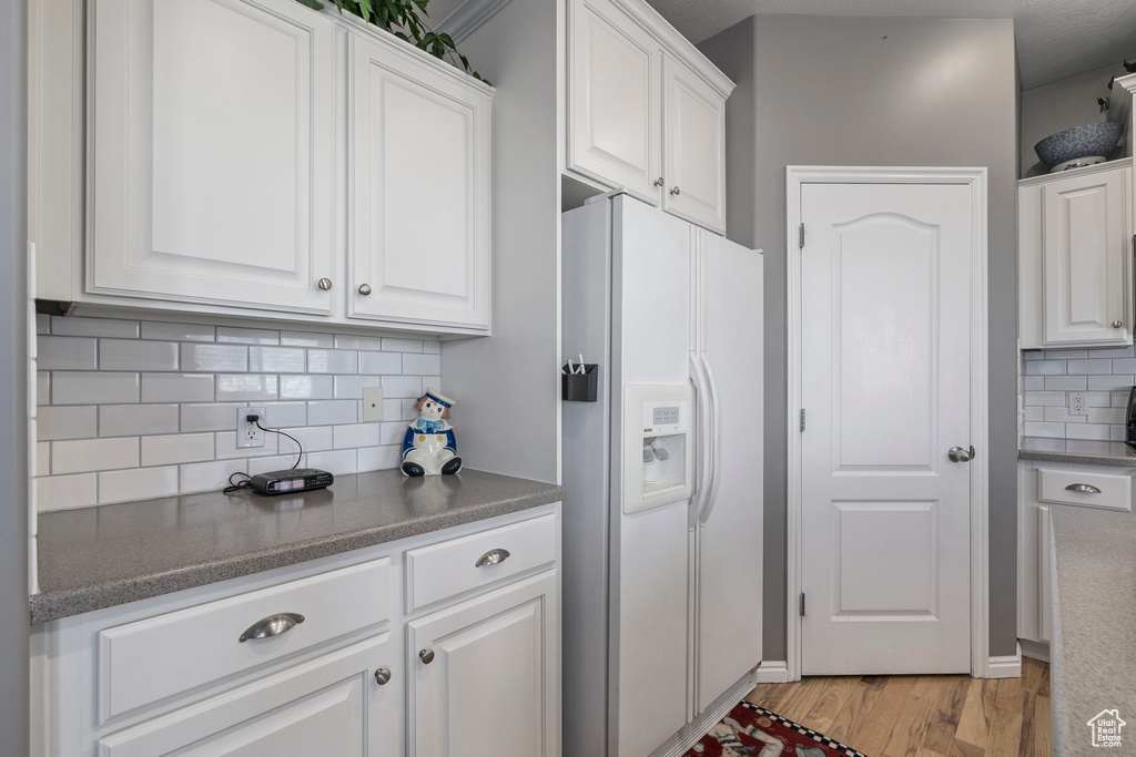 Kitchen featuring white cabinets, backsplash, white refrigerator with ice dispenser, and light hardwood / wood-style flooring