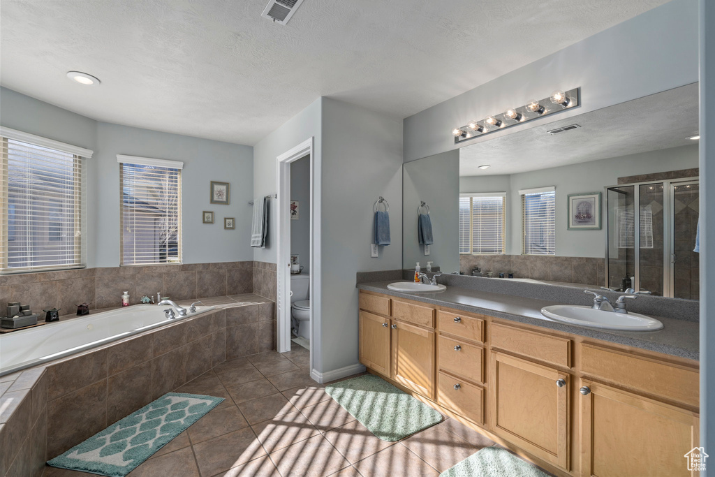 Full bathroom with toilet, double sink, vanity with extensive cabinet space, separate shower and tub, and tile floors