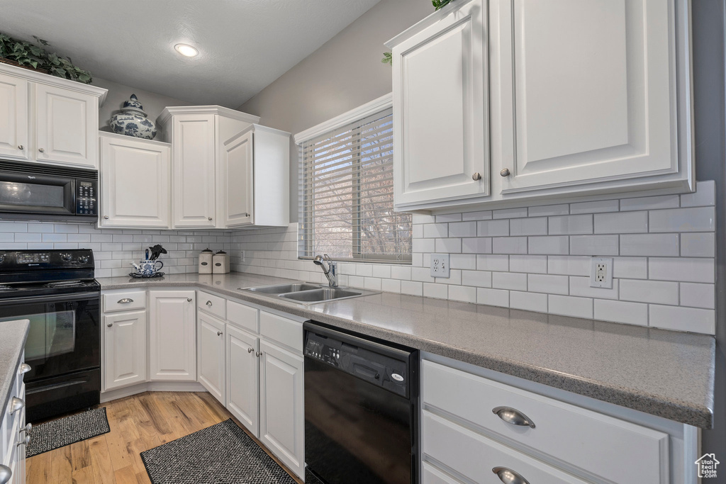 Kitchen featuring black appliances, white cabinets, backsplash, light wood-type flooring, and sink