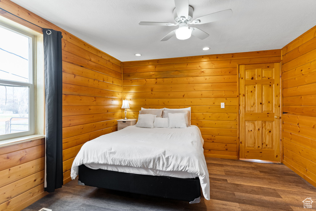 Bedroom with dark hardwood / wood-style floors, wooden walls, and ceiling fan