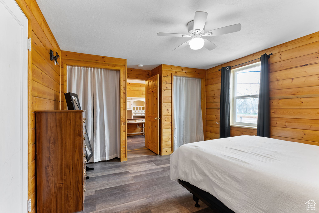 Bedroom with dark wood-type flooring, wood walls, and ceiling fan