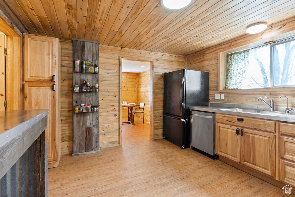 Kitchen with sink, black refrigerator, dishwasher, wood walls, and light wood-type flooring