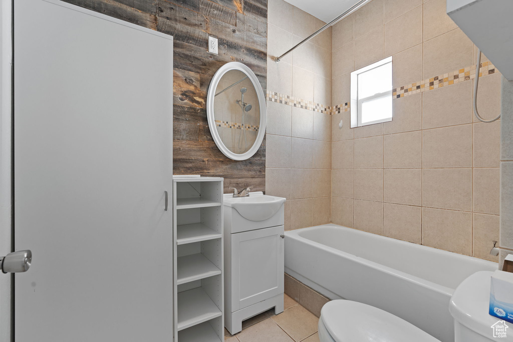 Full bathroom featuring toilet, wood walls, tiled shower / bath combo, vanity, and tile flooring
