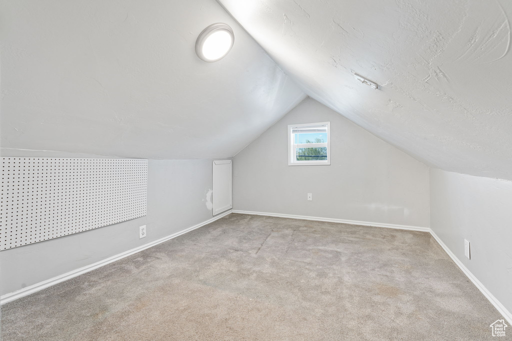 Additional living space with light carpet, vaulted ceiling, and a textured ceiling