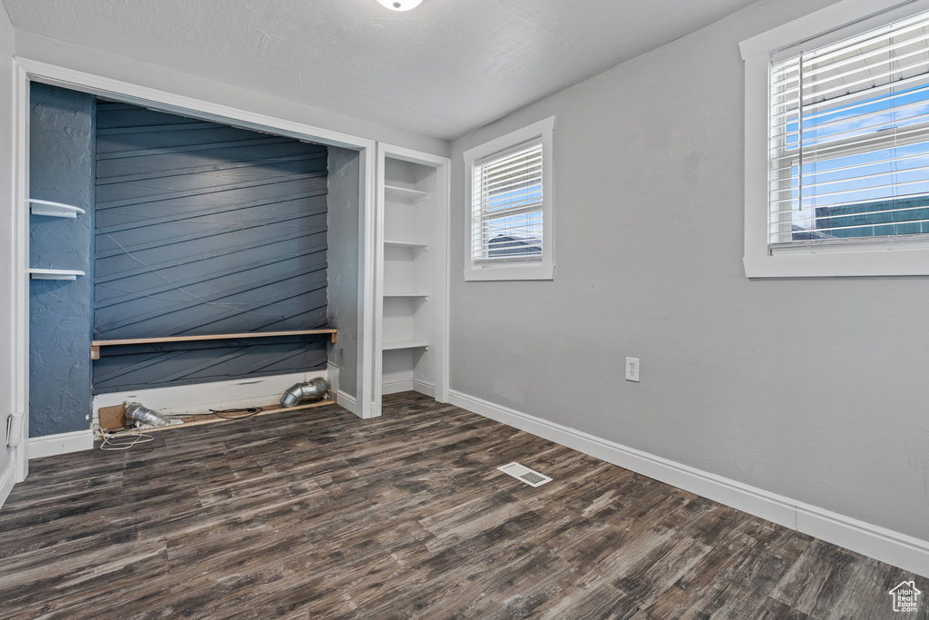 Empty room with plenty of natural light, built in features, and dark wood-type flooring