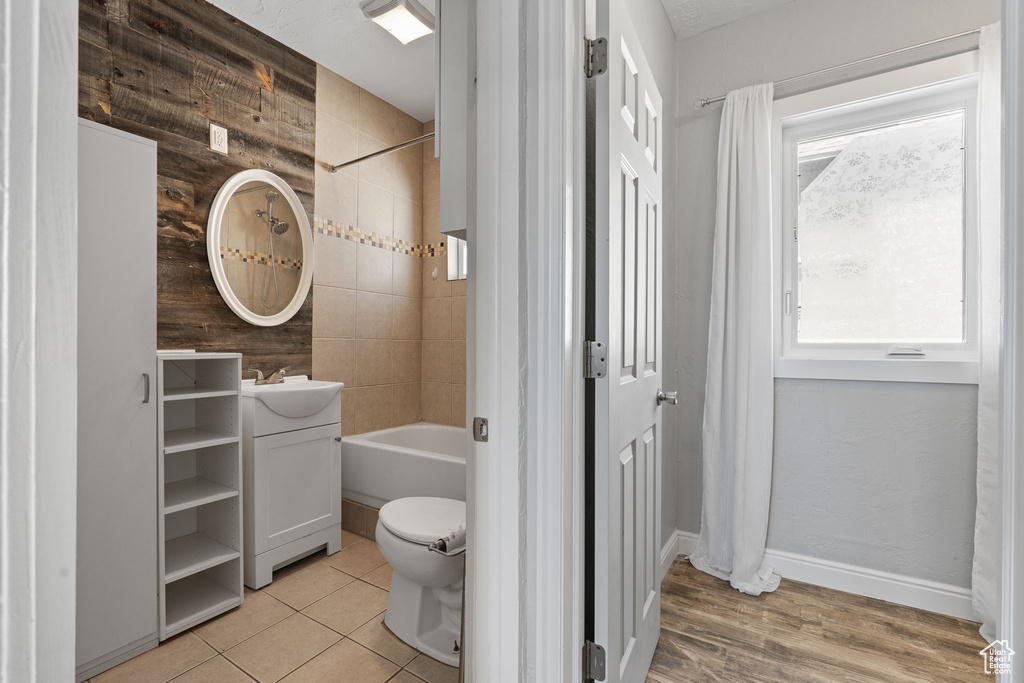 Full bathroom with plenty of natural light, wood walls, shower / bath combo, and hardwood / wood-style floors